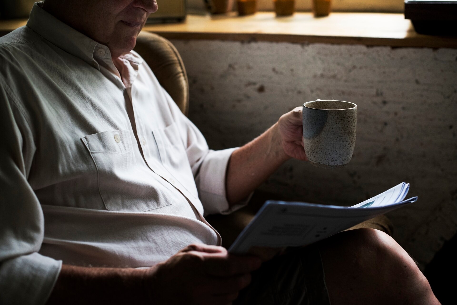 Man i fåtölj läser ett utskrivet dokument med en kaffemugg i handen