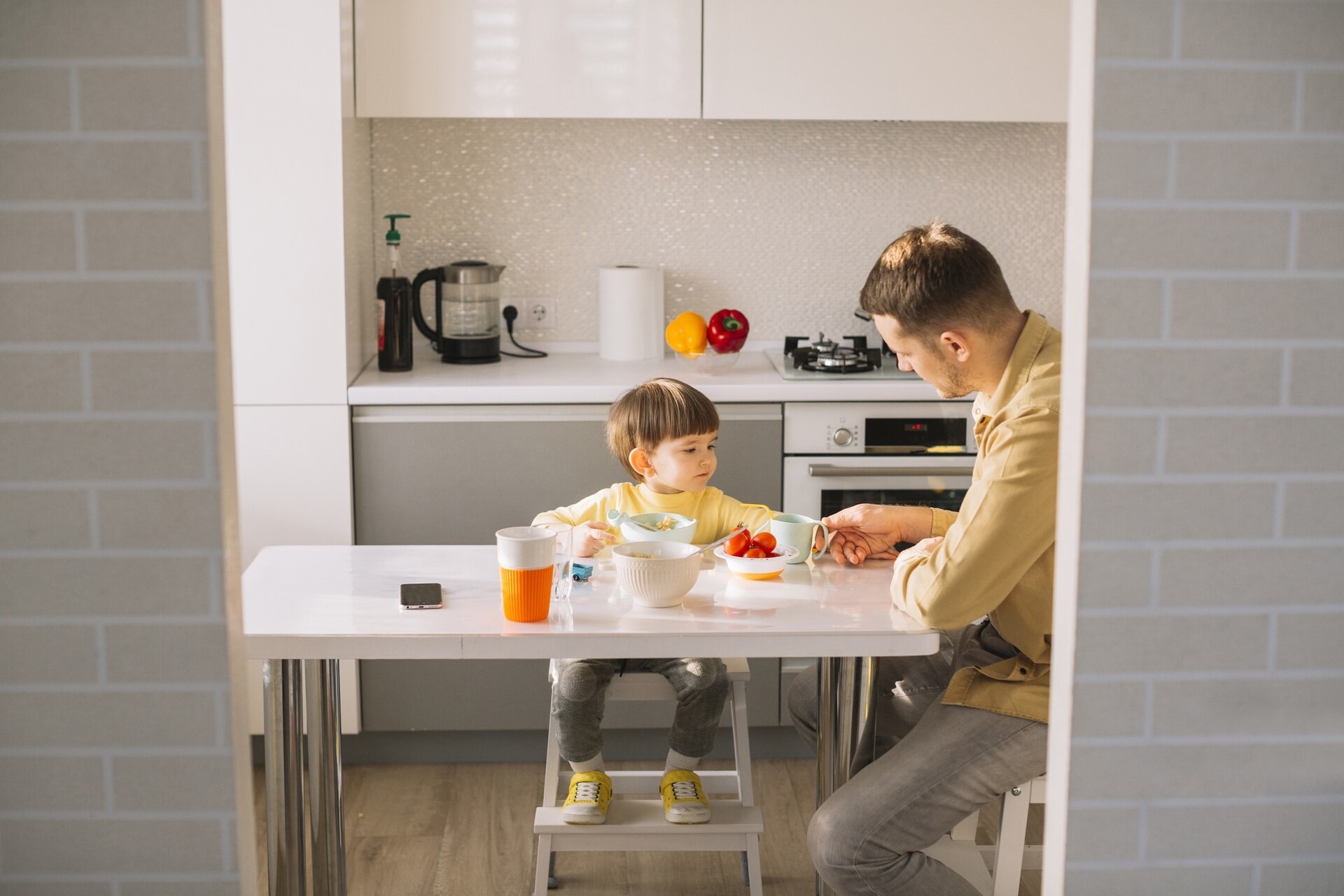 Litet barn på en hög stol med fotstöd äter vid köksbordet med sin pappa